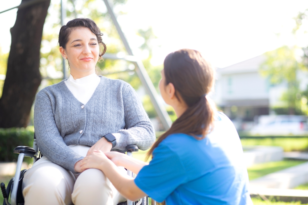 Young Caucasian Nurse Comforting With Patient While Sitting On Wheelchair
