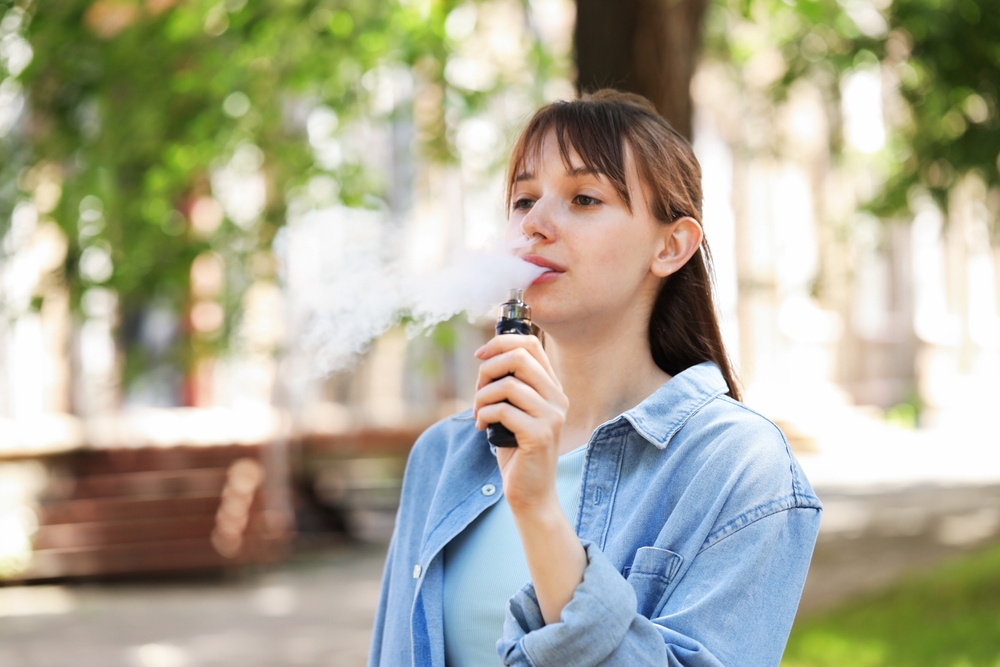 Young Woman Using Electronic Smoking Device Outdoors Space For Text