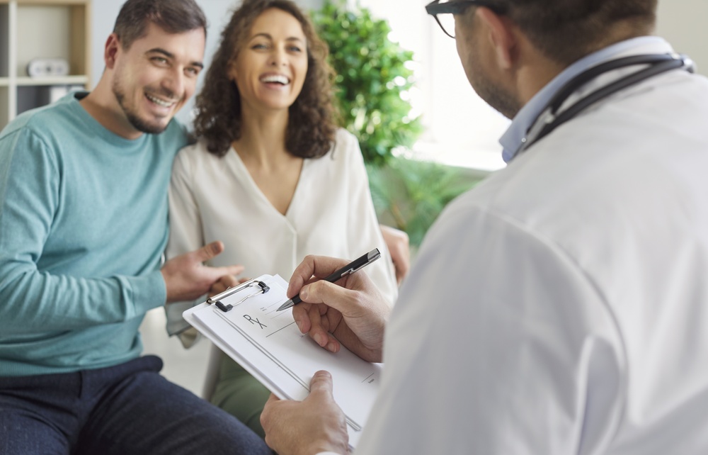 Male Family Doctor In Medical White Uniform Sitting With Report