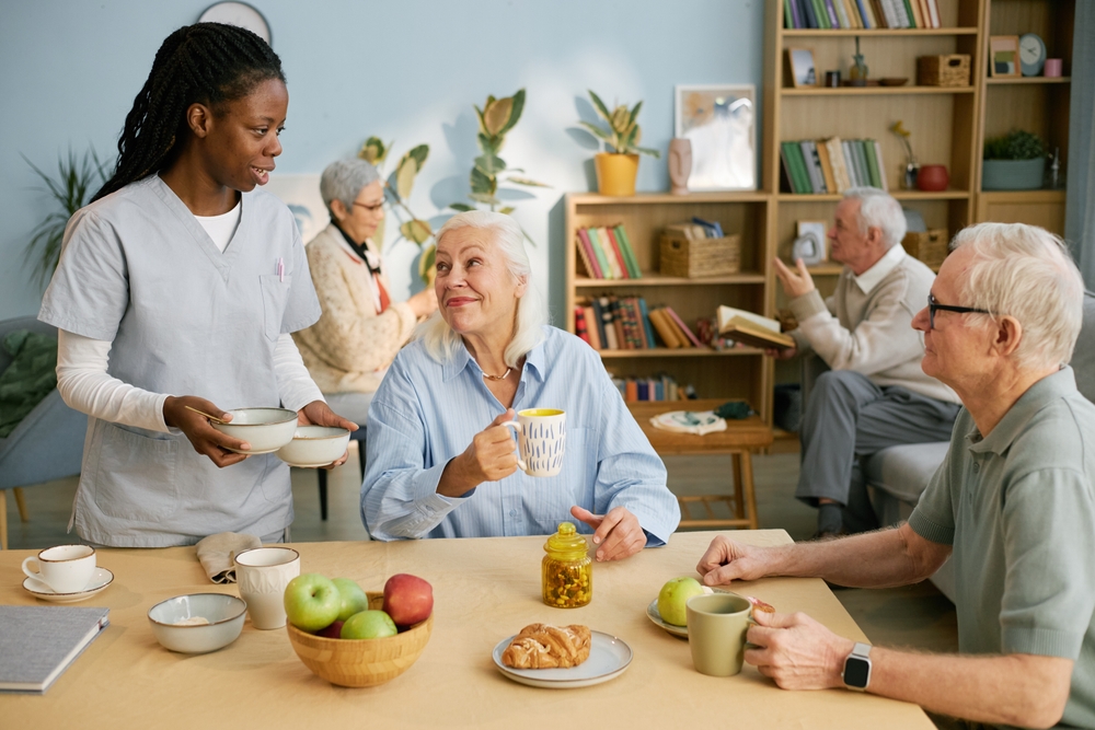 Caregiver Serving Tea And Snacks To Seniors In Cozy Community