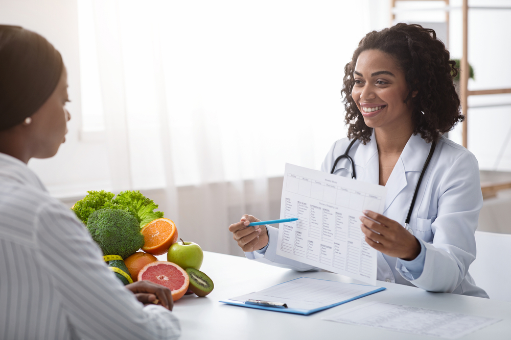 Smiling African Doctor Dietologist Showing Patient Woman Treatment Plan