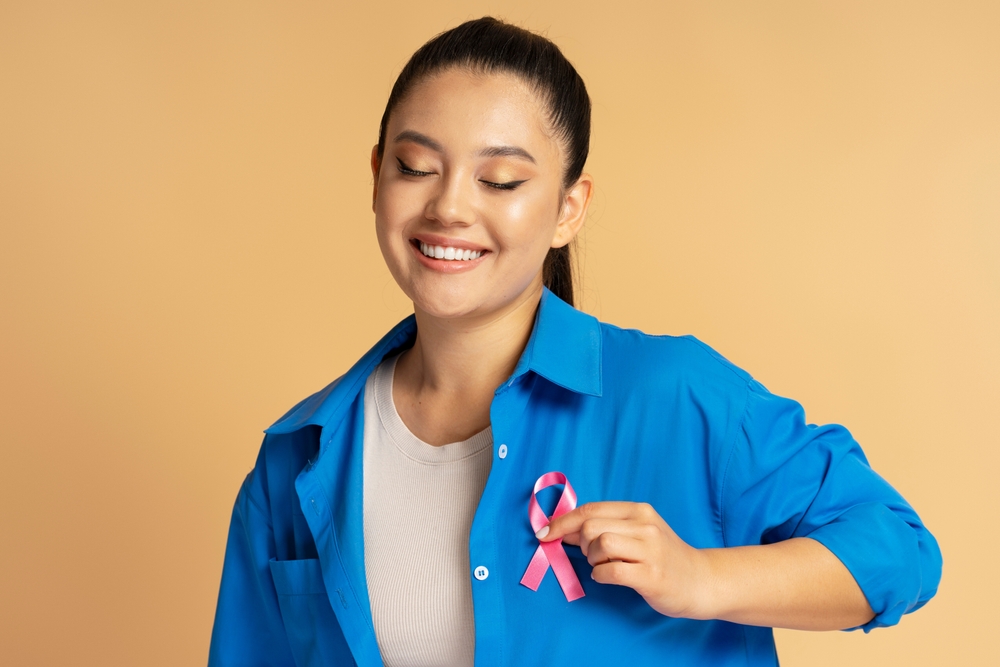 Asian Woman Smiling And Showing Pink Ribbon Pinned Blue