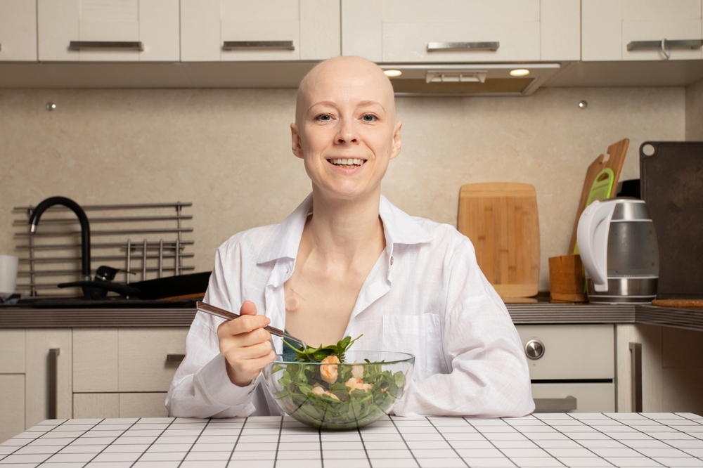 Bald Woman After Cancer Treatment Smiling At Kitchen Table With