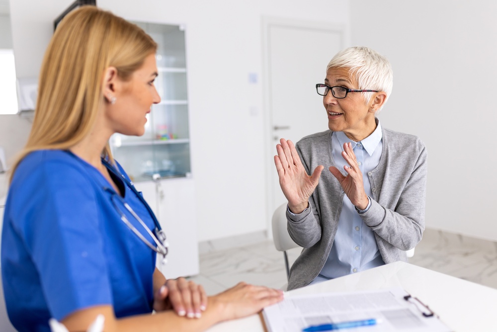 Senior,Woman,Explaining,Symptoms,To,Female,Doctor,In,Blue,Scrubs